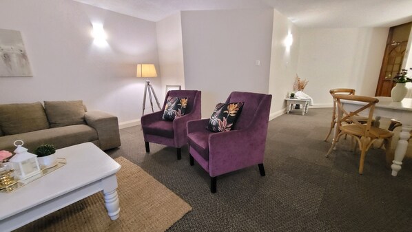 A living room with a sofa, two purple armchairs with floral cushions, a white coffee table, and a small side table with a lamp. - Effortless Homes (East London)