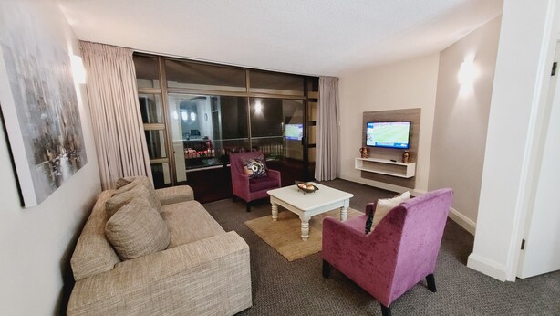 A modern living room with a sofa, armchair, and a television on a stand. - Effortless Homes (East London)