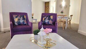A room with two purple armchairs with floral cushions, a white table with a gold tray, a small potted plant, and a vase with a pink flower. - Effortless Homes (East London)