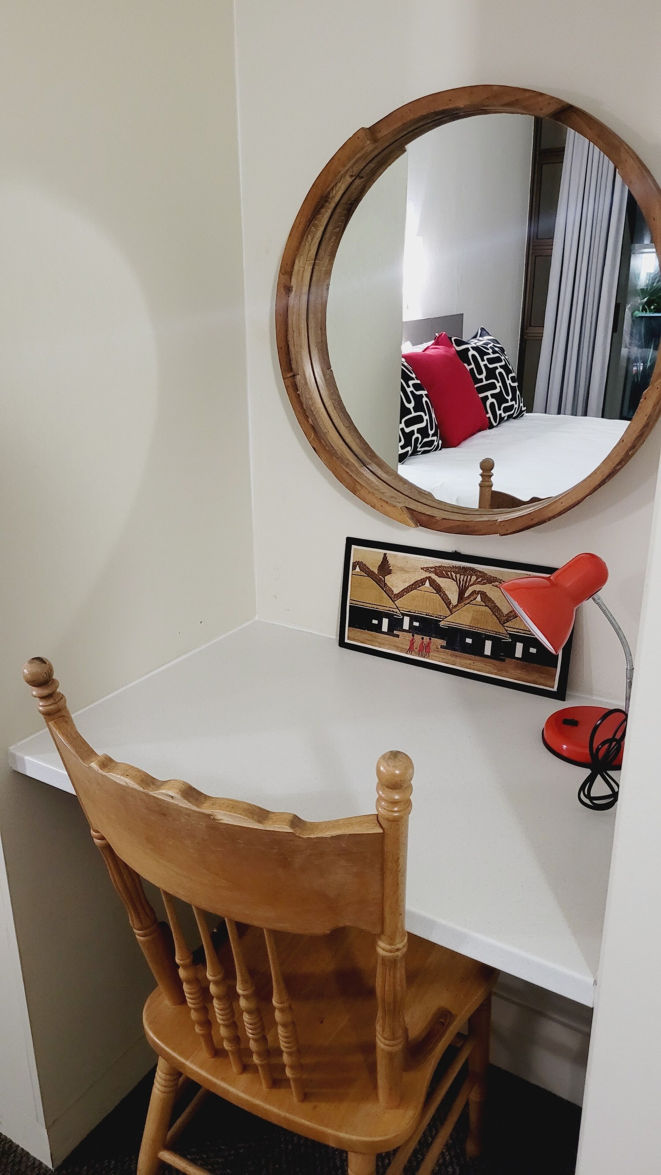 A wooden chair with a high backrest and armrests, a white desk, a round mirror, and a framed picture on the wall.
