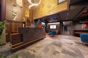 A reception area with a wooden reception desk, a blue chair, and a wall-mounted screen displaying a logo.