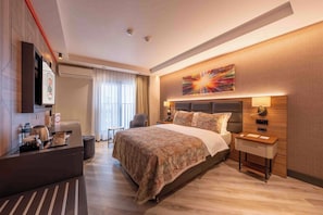 A hotel room with a bed, bedside table, wall-mounted TV, and a desk with a chair.