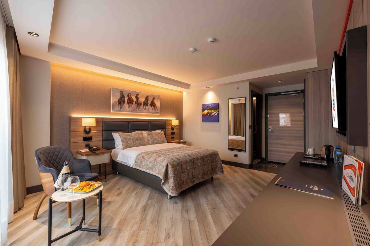 A hotel room with a bed, bedside table, chair, and a small table with a tray of food.
