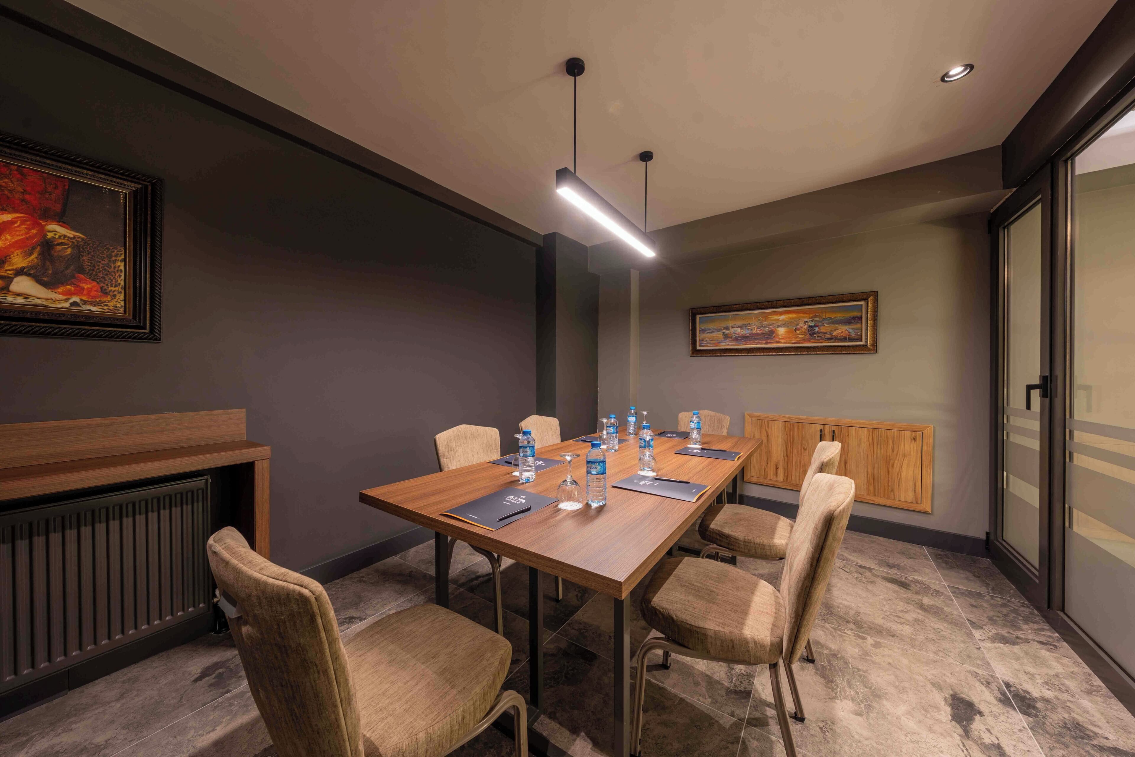 A conference room with a long table, chairs, water bottles, and a painting on the wall.