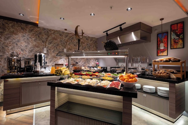 Un bufé con diversas opciones de comida, una estación de café y una pared decorativa con motivos florales.