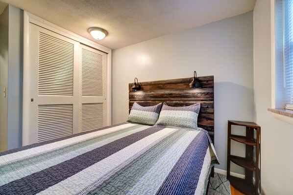 A bedroom with a striped bedspread, wooden headboard, and a bedside table. - Roomy 4BR home in West Knox w/ Patio - 6mi from UT (Knoxville)