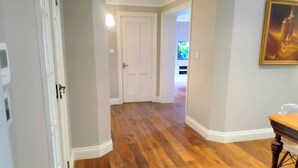 A hallway with wooden flooring, white walls, and a dining table with chairs.