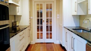 A kitchen with white cabinets, a wooden floor, a double door with glass panels, and a stainless steel sink.