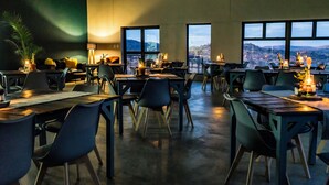 A spacious dining area with multiple tables and chairs, large windows offering a view of the mountains, and ambient lighting. - Stofpad Namibia (Solitaire)