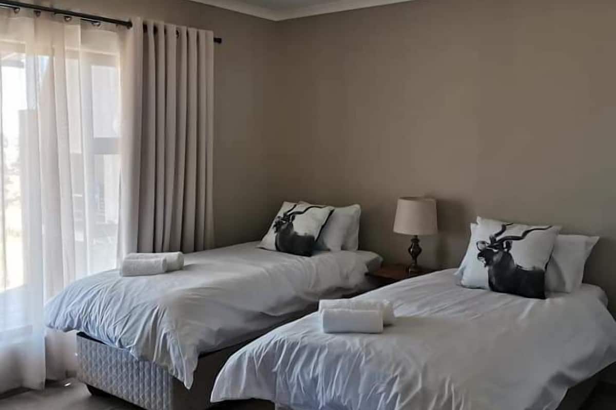 A hotel room with two beds, a window with curtains, a bedside table with a lamp, and a striped rug.