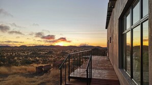 A wooden deck with a metal railing leading to a building with large windows. - Stofpad Namibia (Solitaire)
