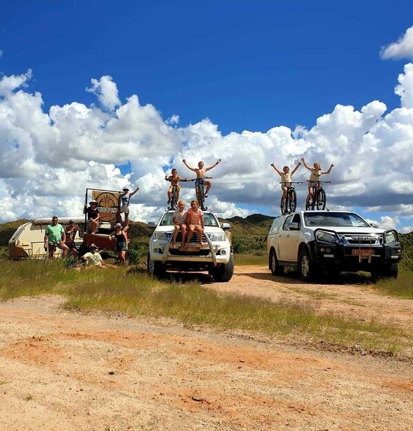 A group of people on bicycles and a vehicle parked on a dirt road with a clear sky. - Stofpad Namibia (Solitaire)