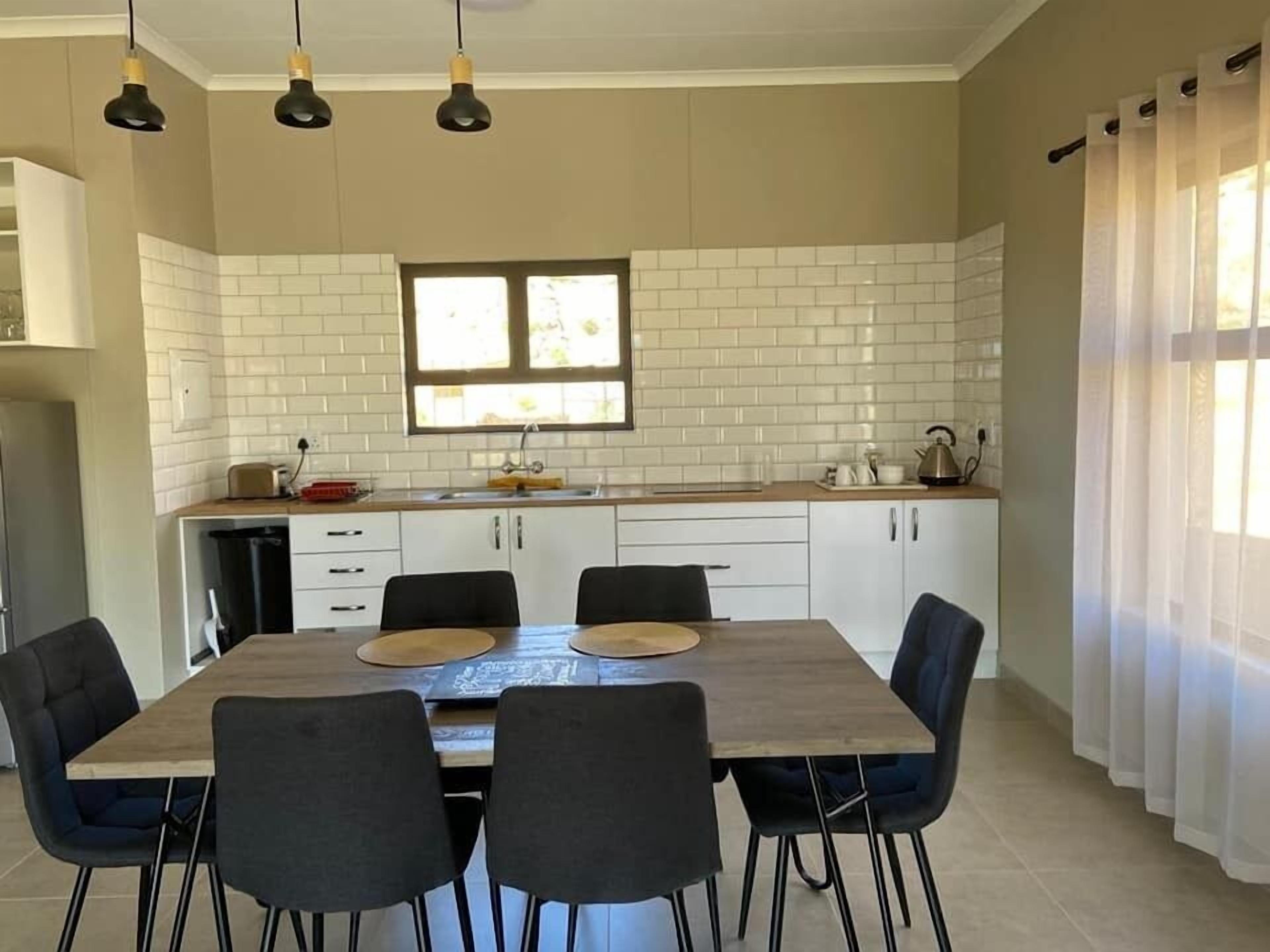 Une cuisine moderne avec des carreaux de céramique blancs disposés en motif métro, une table à manger en bois avec quatre chaises et une fenêtre avec des rideaux.