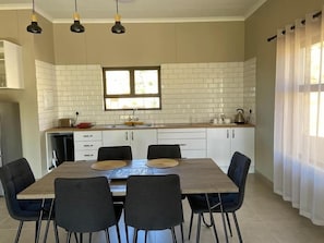 A modern kitchen with white subway tiles, a wooden dining table with four chairs, and a window with curtains.