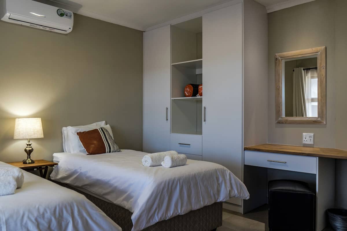 A hotel room with two beds, a desk, a wardrobe, and a mirror.
