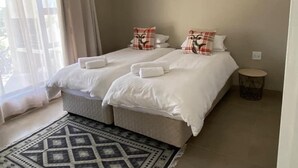 A double bed with white bedding and decorative pillows, a small round table, and a patterned rug. - Stofpad Namibia (Solitaire)