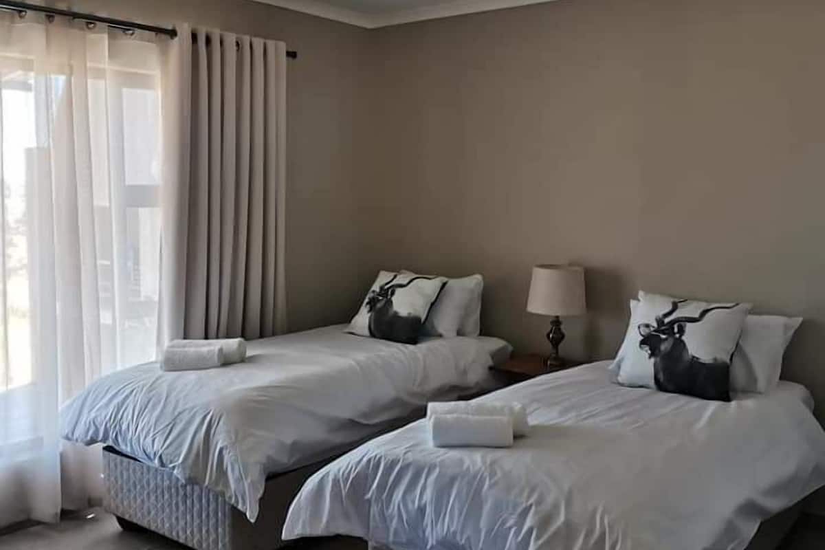 A hotel room with two beds, a window with curtains, a bedside table with a lamp, and a rug on the floor.