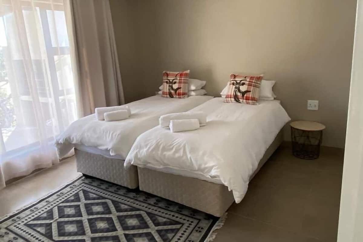 A bedroom with two beds, a patterned rug, and a small round table.