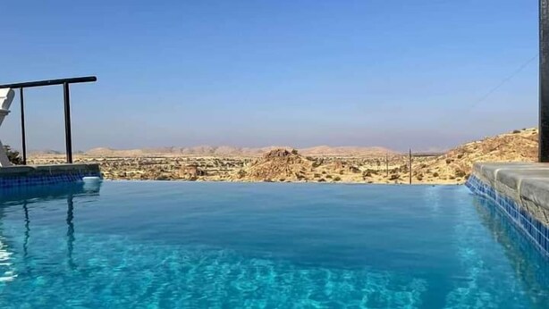 A clear blue infinity pool with a view of a desert landscape. - Stofpad Namibia (Solitaire)