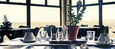 A dining table set with plates, cutlery, glasses, and a potted plant.