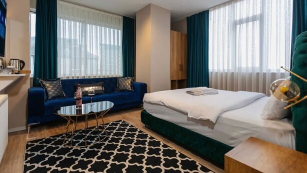 A hotel room with a bed, a sofa, a coffee table, and a TV. - Lina Suit Hotel (Istanbul)