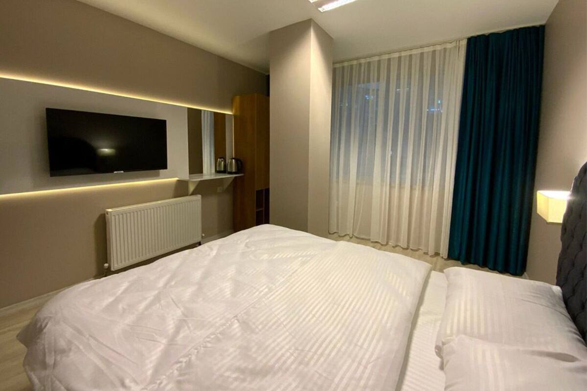 A hotel room with a large bed, a flat-screen TV mounted on the wall, a window with curtains, and a radiator.