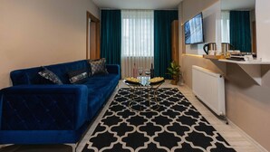A modern living room with a blue sofa, a patterned rug, and a dining table with a tray of snacks. - Lina Suit Hotel (Istanbul)