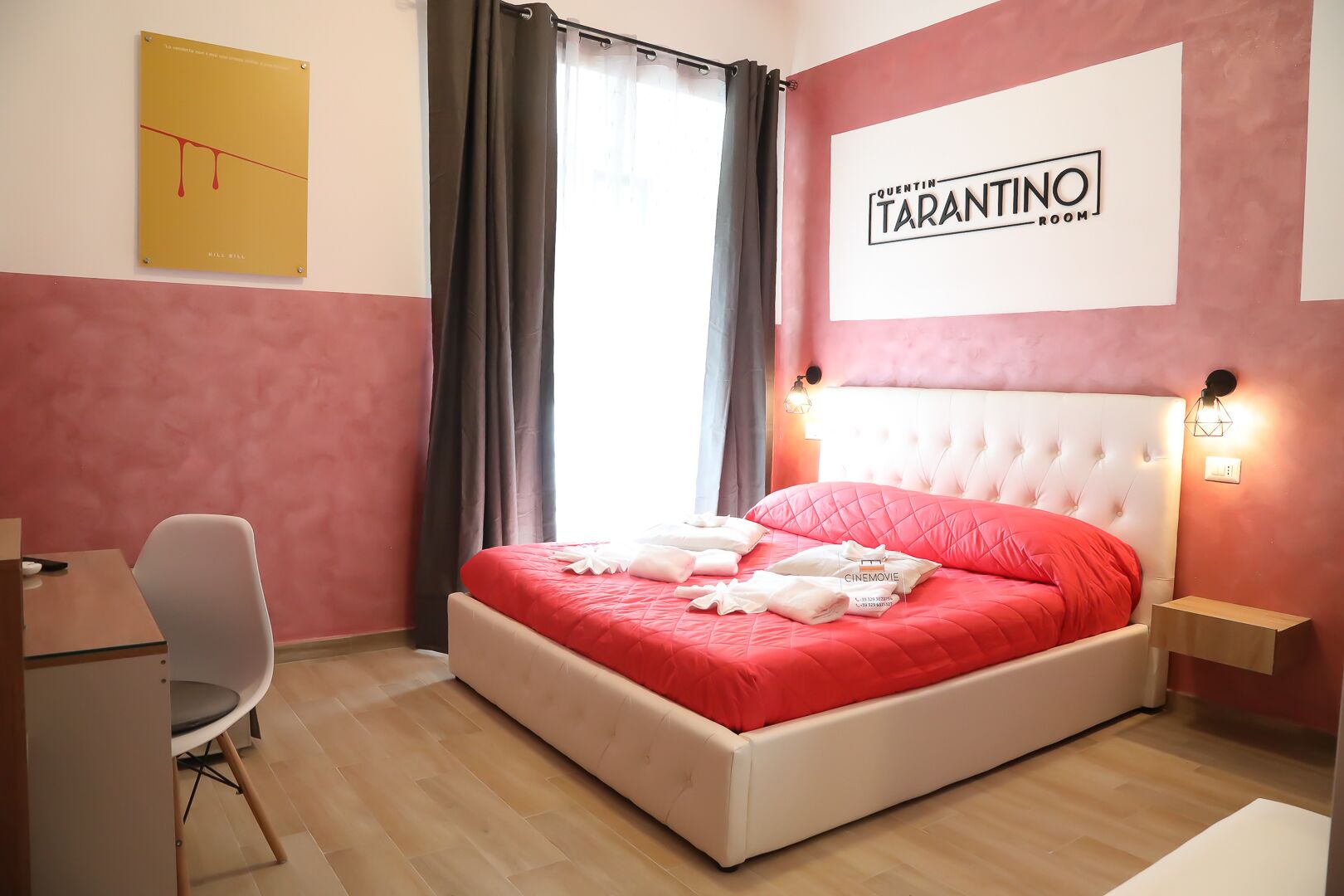 Habitació d'hotel amb un llit, un escriptori i una cadira. La habitació té un cartell que diu "Quentin Tarantino Room".
