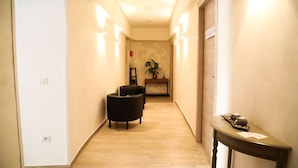 A hotel hallway with a wooden floor, two black armchairs, a small table with a teapot and cups, and a plant. - Cinemovie Guesthouse (Rome)