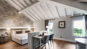 A bedroom with a large bed, a desk, and chairs, a window with curtains, and a ceiling with exposed beams.