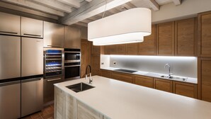 A modern kitchen with stainless steel appliances, a central island with a sink, wooden cabinets, and a pendant light.