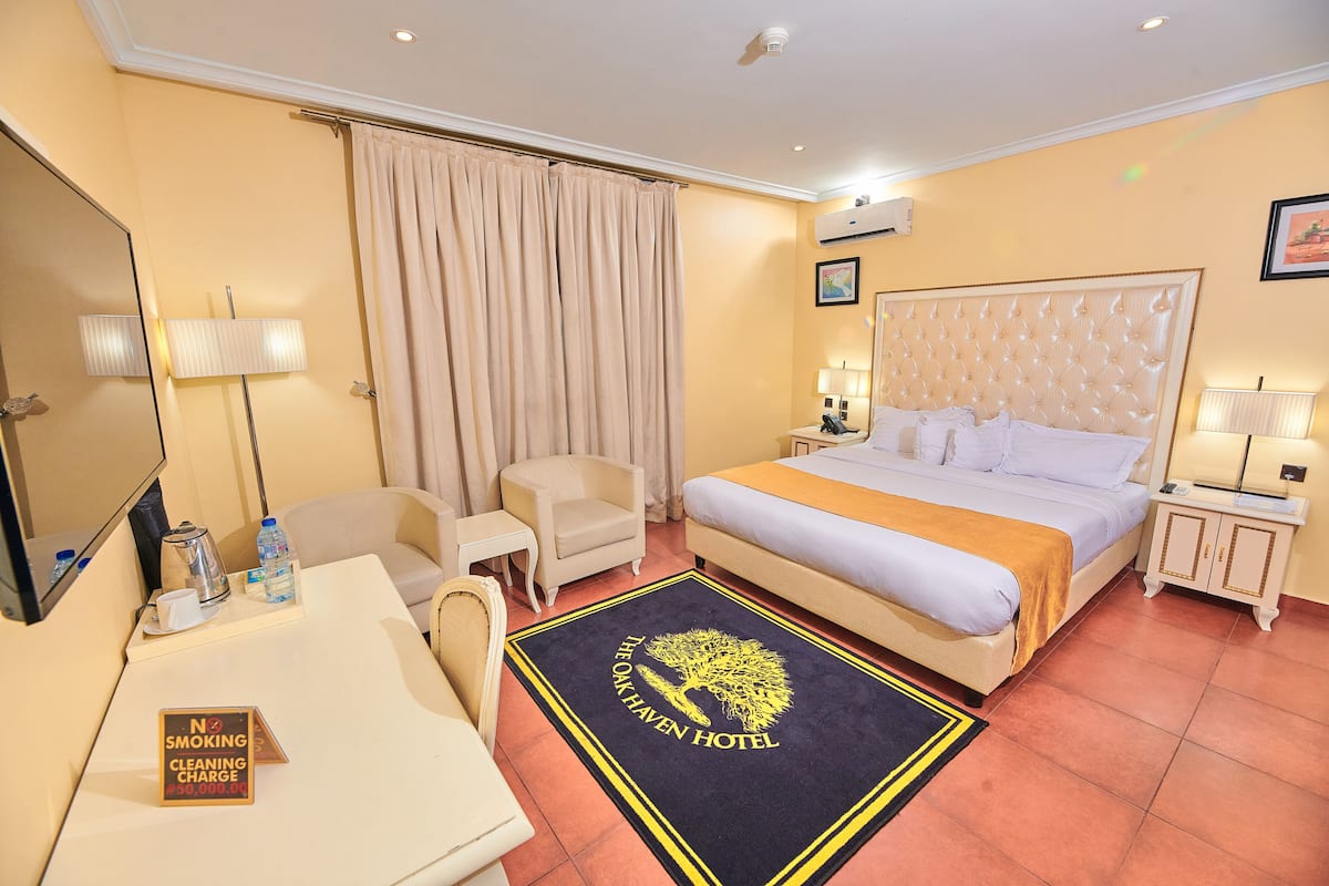 A hotel room with a bed, a desk, a chair, a nightstand, a lamp, and a sign indicating no smoking and no cleaning charge.