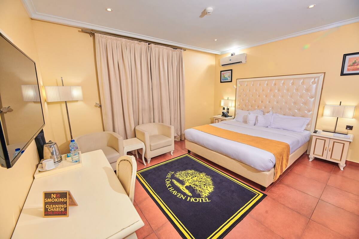 A hotel room with a bed, bedside tables, a desk, a chair, a lamp, a mirror, curtains, and a 'No Smoking' sign.