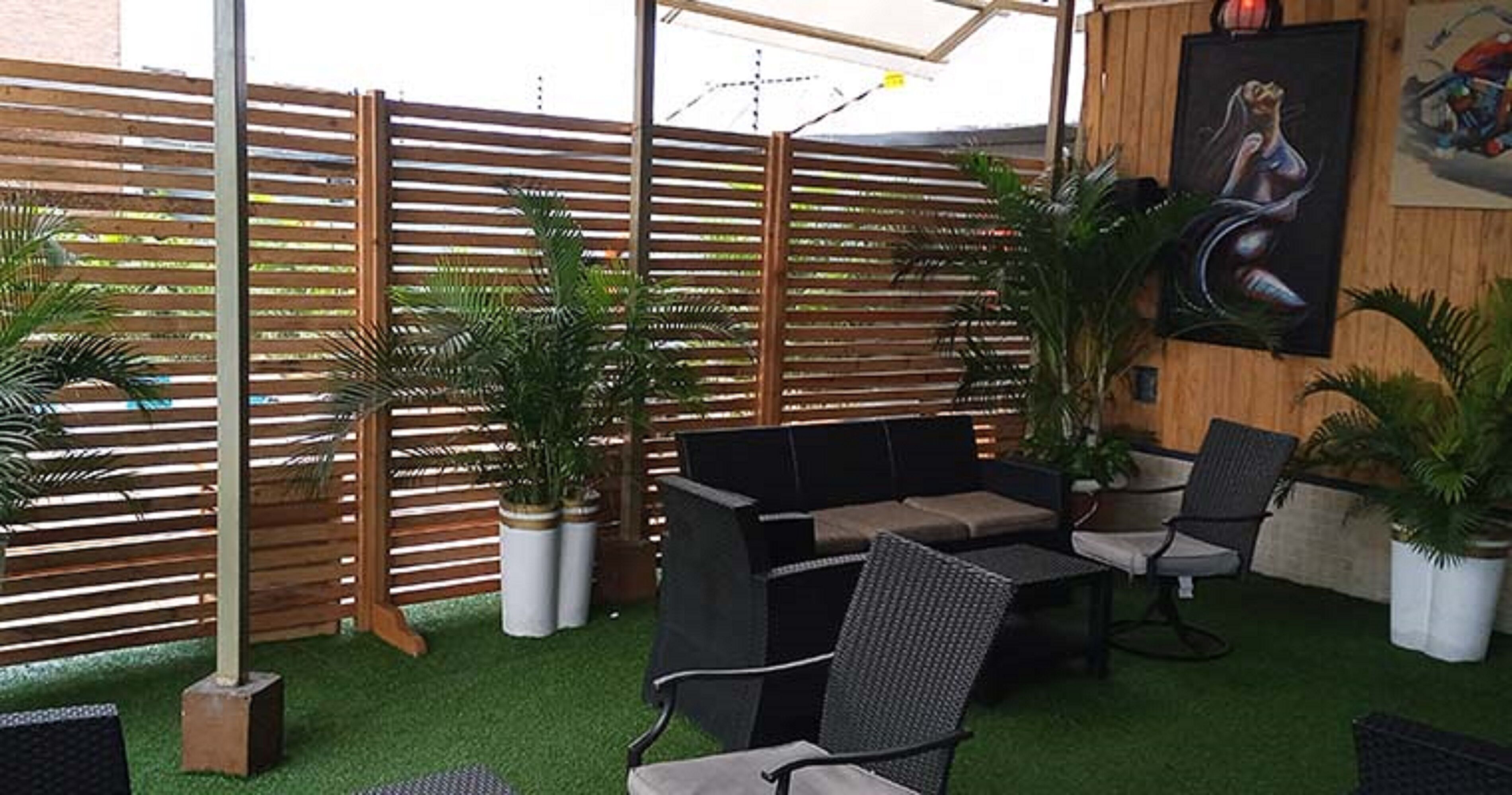 An outdoor patio with a wooden fence, artificial grass, and seating arrangements.