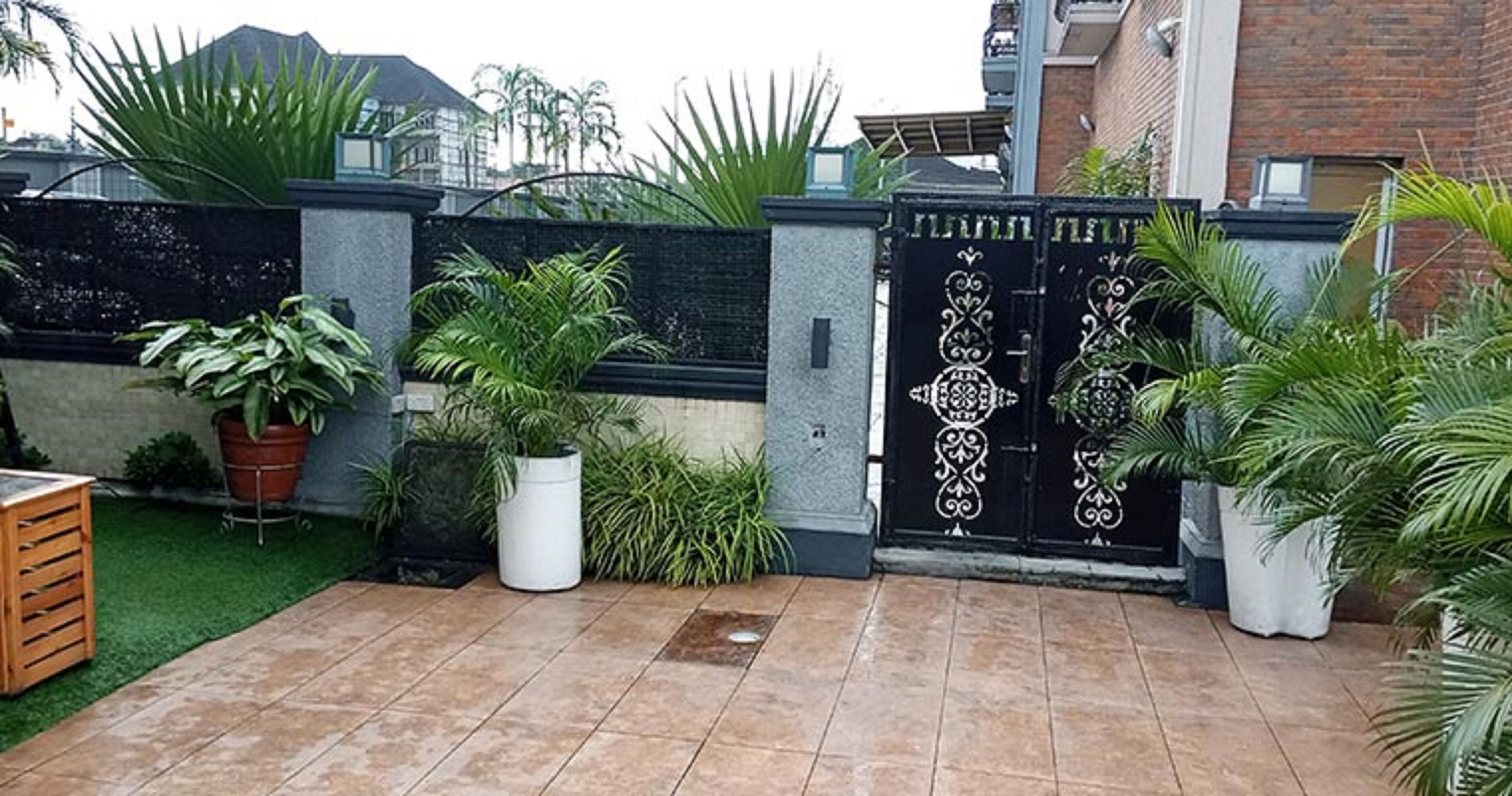 A gated patio area with a tiled floor, surrounded by potted plants and a decorative gate.