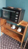 A compact kitchenette with a microwave, a small shelf with cups and glasses, and a patterned floor.