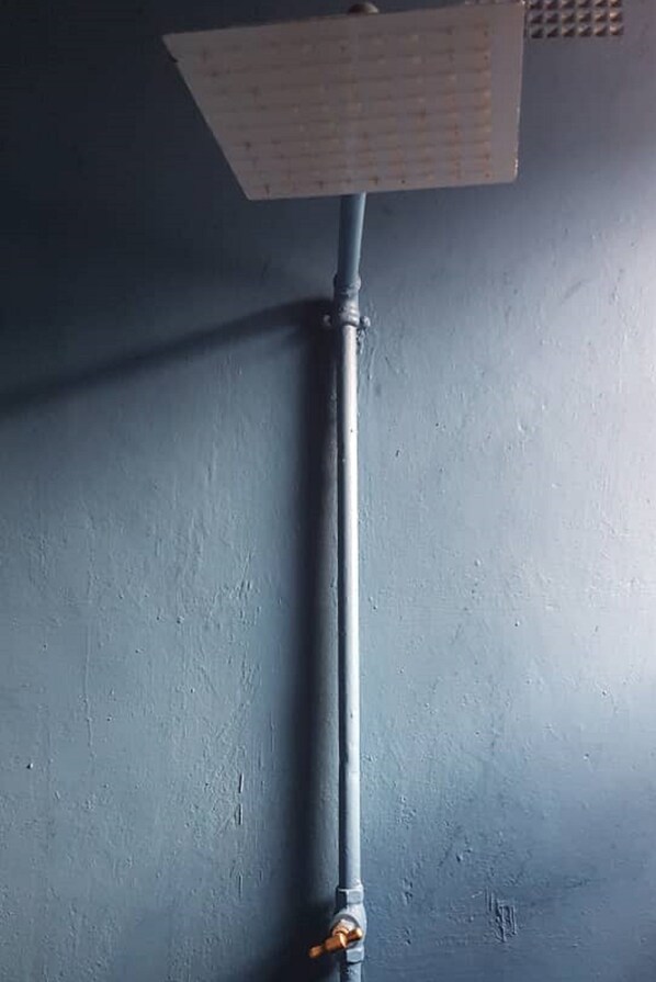 A vertical pipe with a valve and a ceiling-mounted fixture against a plain wall.