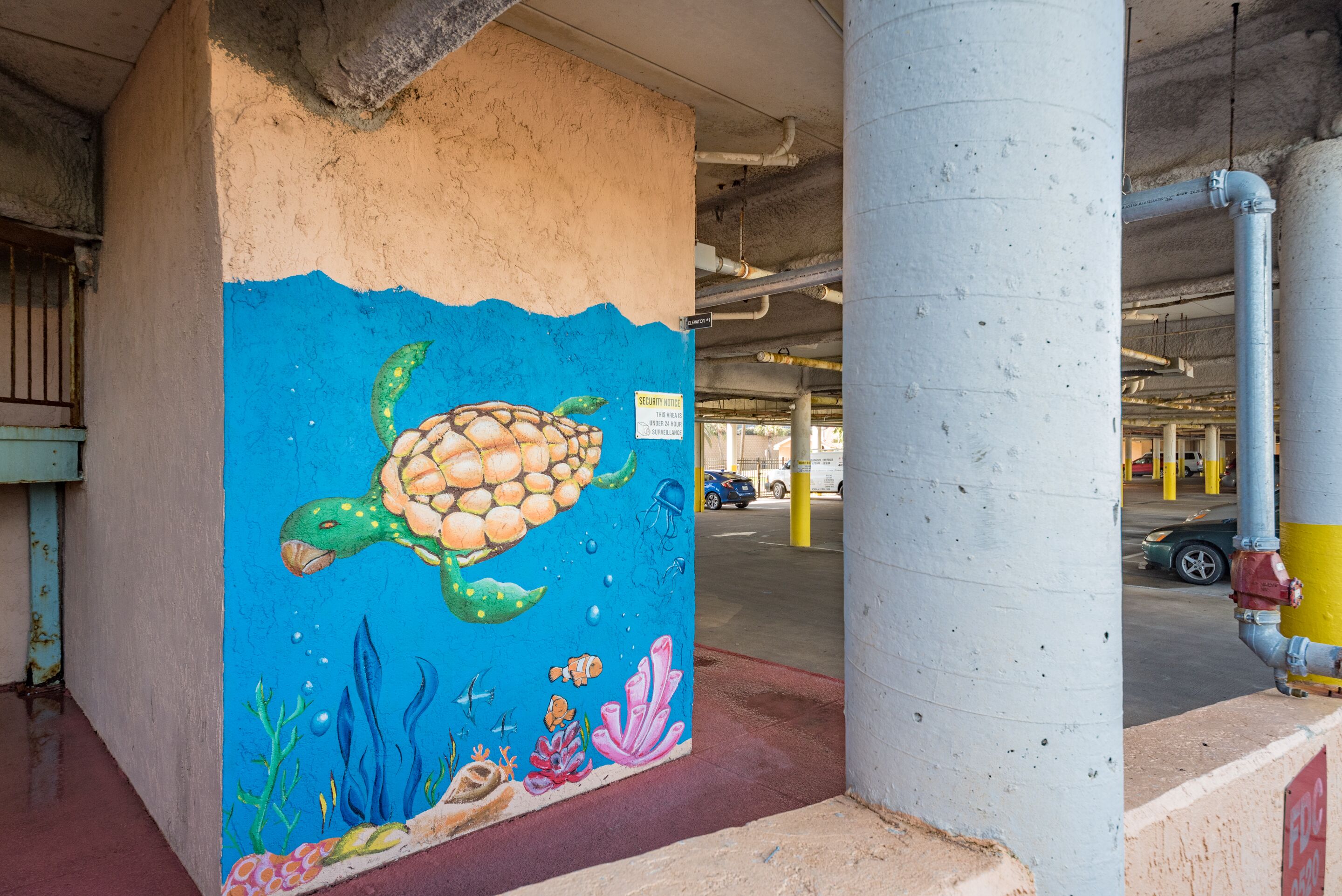 A mural of a turtle on a concrete pillar in a parking garage.