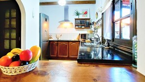 Une cuisine avec des meubles de rangement en bois, un plan de travail noir, un panier de fruits et une fenêtre avec des rideaux.