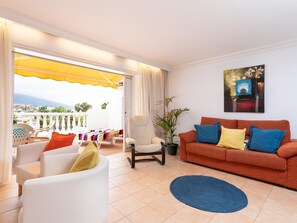 A living room with a sofa, armchairs, a coffee table, a balcony with a yellow awning, and a painting on the wall. - Holiday Home in Puerto de la Cruz (Puerto De La Cruz)
