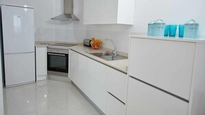 A modern kitchen with white cabinets, a stainless steel range hood, a built-in oven, a sink, and a countertop with fruit and storage containers. - Beautiful holiday home with sea views +beach+WIFI (El Rosario)