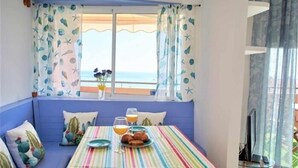A room with a striped table set for breakfast, a window with a view of the sea, and a blue bench with cushions. - Beautiful holiday home with sea views +beach+WIFI (El Rosario)