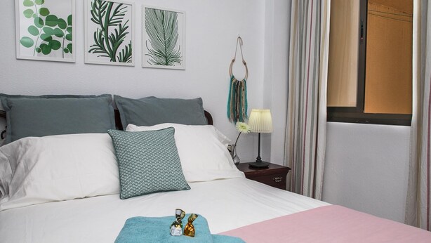 A neatly made bed with a pink bedspread and a teal blanket, a bedside table with a lamp and decorative items, and three framed botanical prints on the wall. - Confortable vivienda en La Laguna a 5 Min tranvía (San Cristobal De La Laguna)