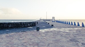 Un paseo empedrado que conduce a un muelle, con un muro de piedra a un lado y boyas azules al otro.