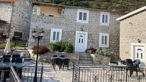 A stone building with a courtyard, outdoor seating, and a mountain backdrop. - Sleeps 8 /9 people. 2 apartments. Pool. Sea and mountain  viewsi (Tivat)