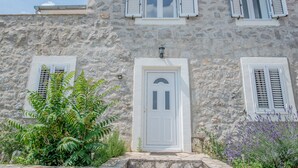 A stone building with a white door, two windows with shutters, and a small lamp above the door. - Sleeps 8 /9 people. 2 apartments. Pool. Sea and mountain  viewsi (Tivat)