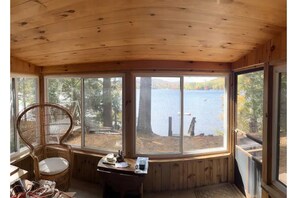 Relax in a cozy cabin room with a scenic lake view, featuring a bay window, wicker chair, and reading nook.