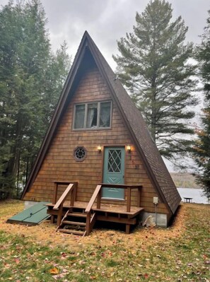 Una cabaña de madera con techo triangular, puerta principal y un pequeño porche con escalones.