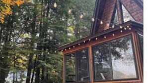 Una cabaña con amplias ventanas, fachada de madera y un leñedo afuera.