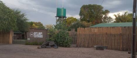 A dirt ground with a sign for 'DITLHAPI COTTAGES' and a water tank.